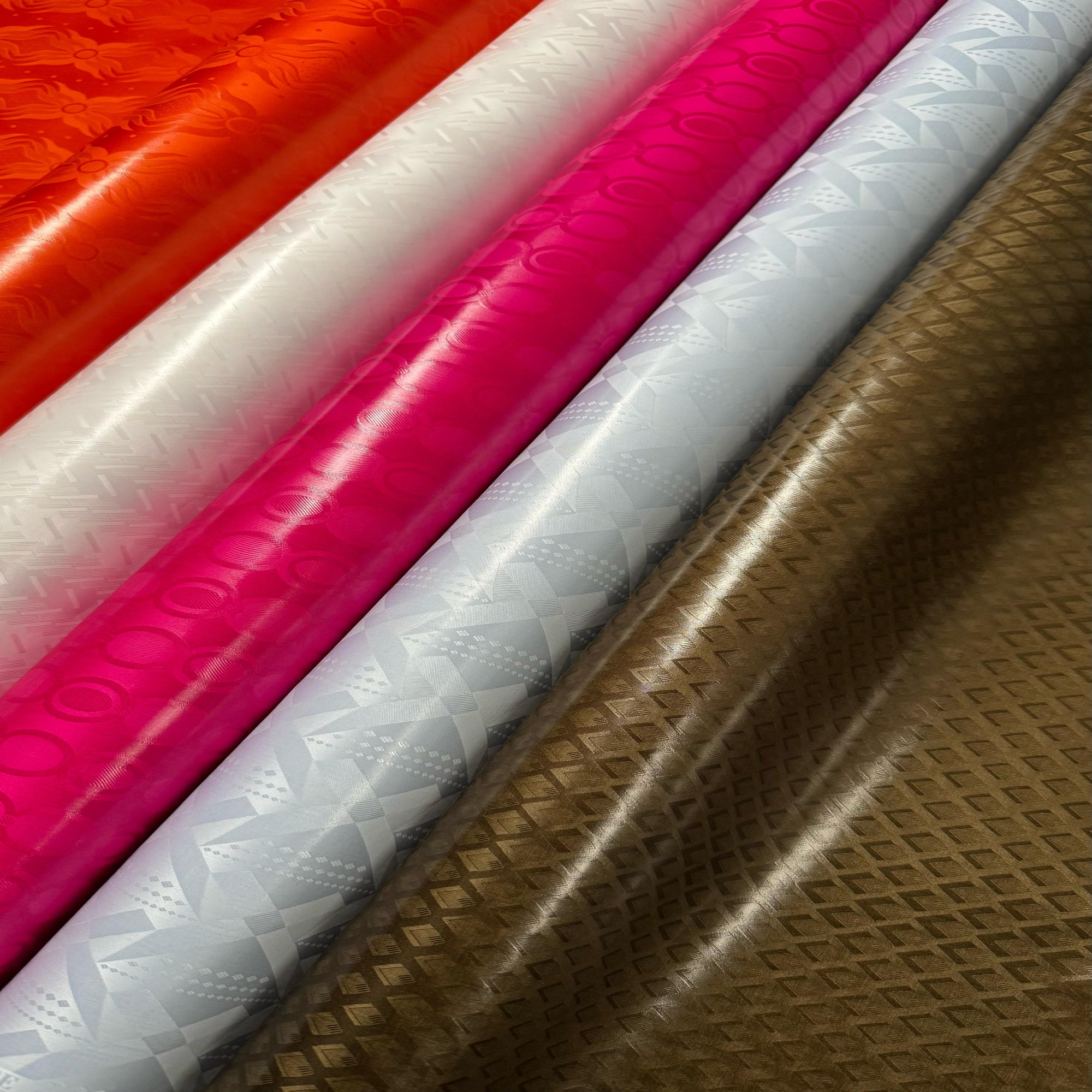 Close-up of Bazin Riche fabric samples in red, white, pink, and brown.